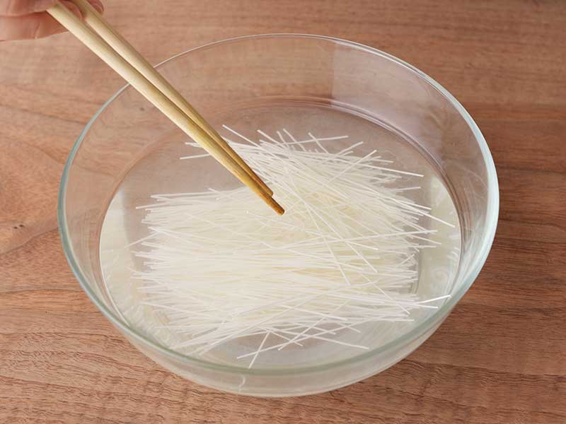 深い耐熱ボウルに湯と半分に折ったそうめんを入れて、そうめんが水面から出ないように箸で沈めます。