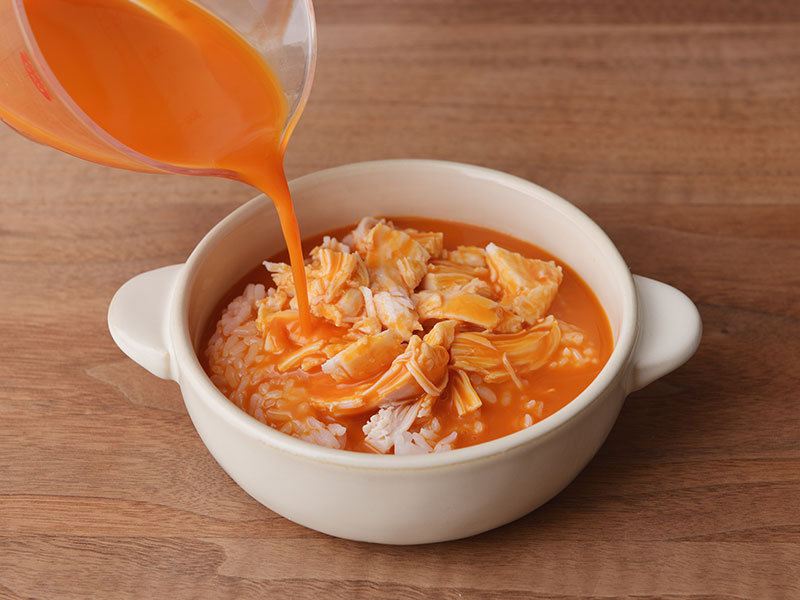 耐熱容器に温めたご飯、手で食べやすい大きさに割いたサラダチキン、野菜ジュース、塩を入れて軽く混ぜ合わせます。