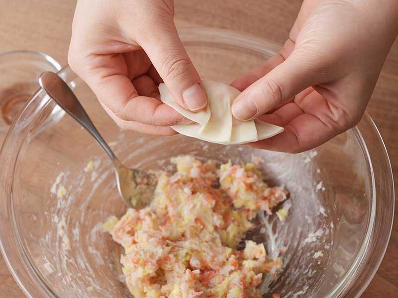 ３のたねを１人７個になるように等分し、餃子の皮にのせます。皮の縁に水(分量外)をつけ、ひだを付けながら閉じます。